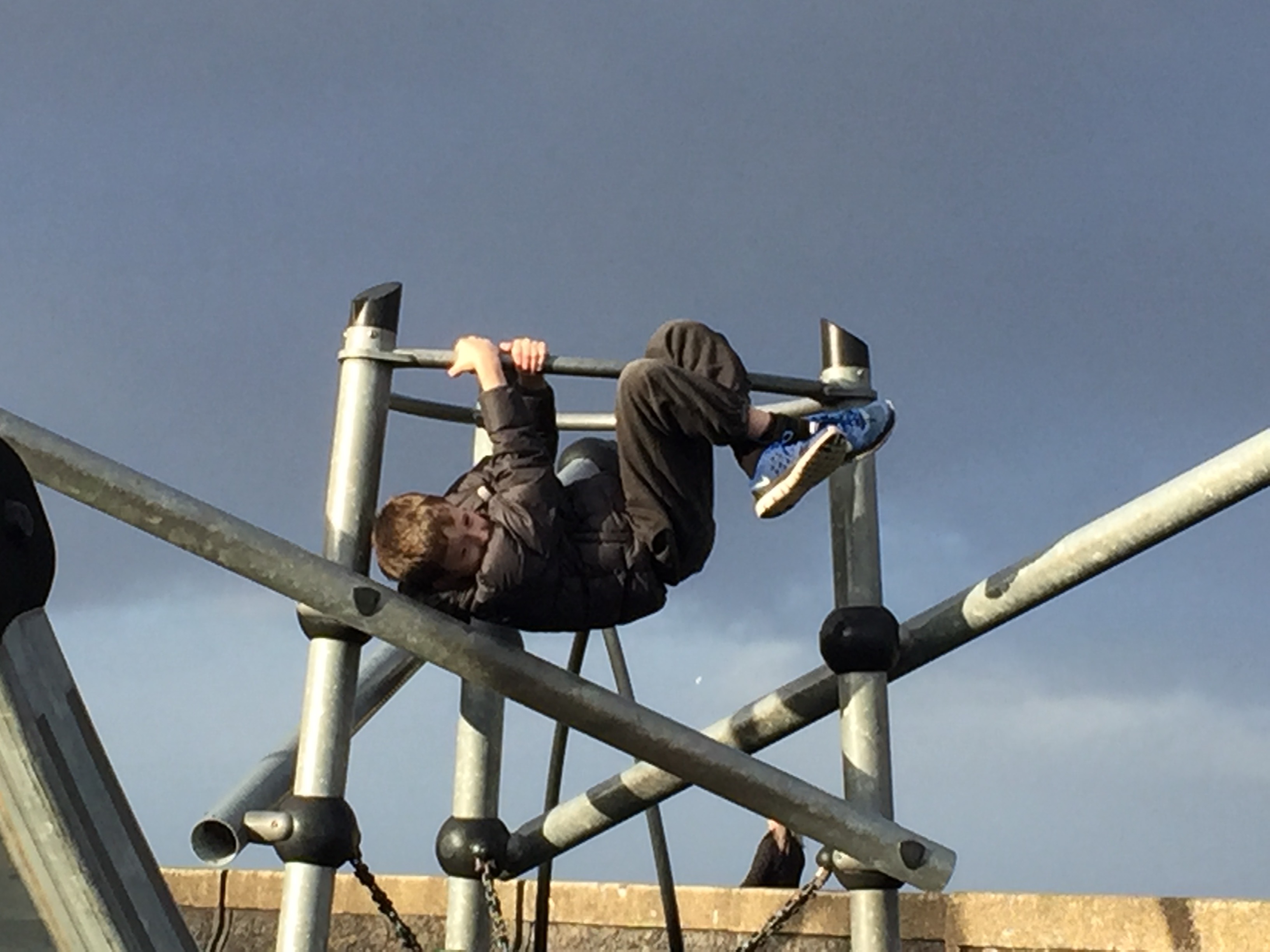 boy hanging from climbing frame